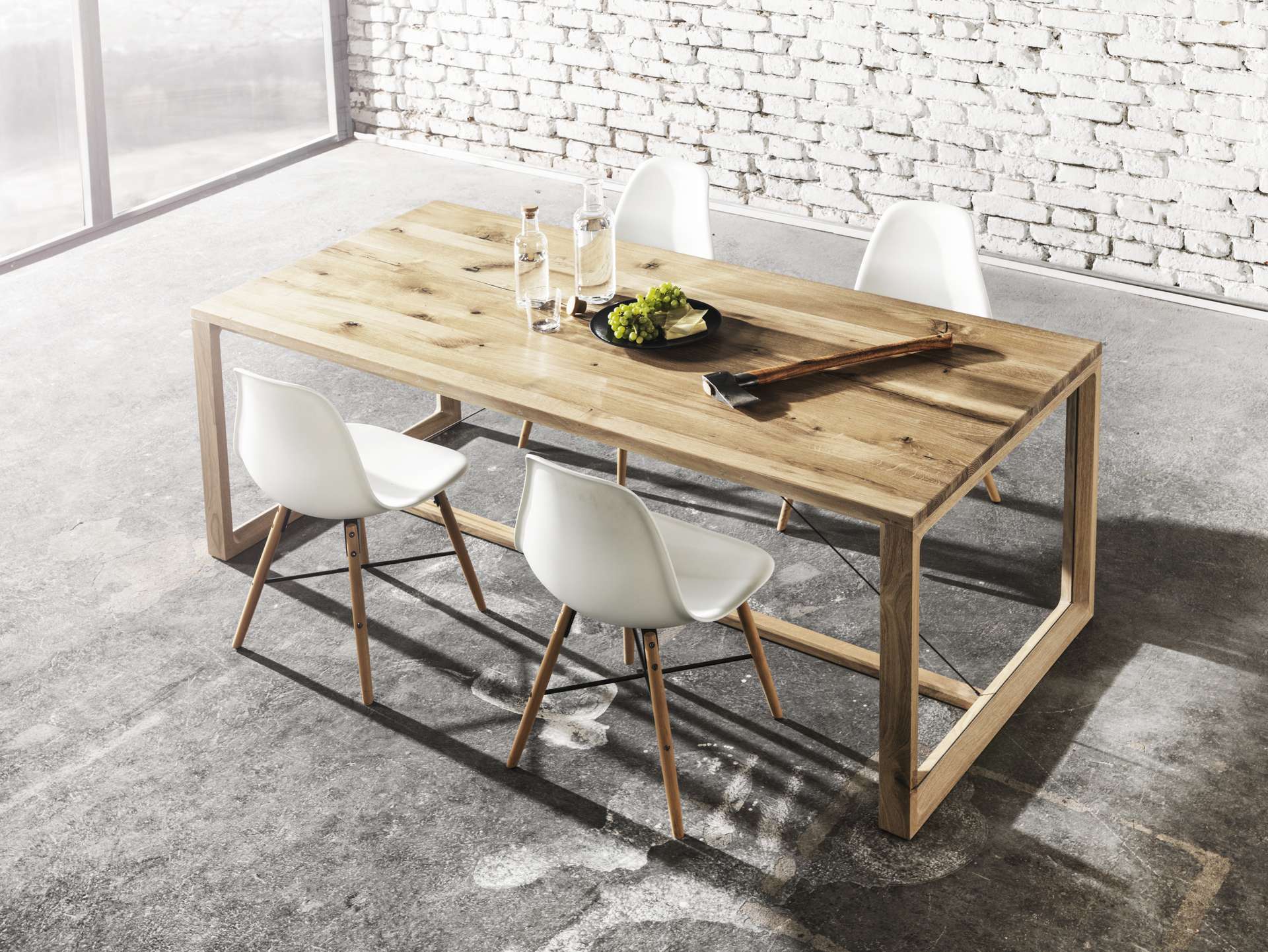 Massivholz Eichentisch mit charaktervollen Tischplatte bestückt mit Designersessel. Der Tisch ist dekoriert mit einer Obstschüssel, Wasserkaraffe und einer Axt.